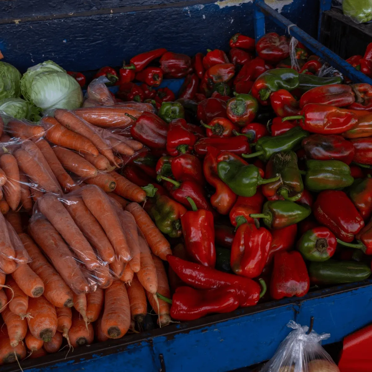 Fresh vegetables: carrots, peppers, and cabbages displayed at a market stall.