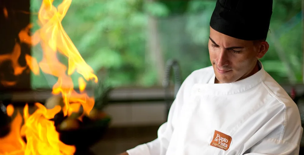 Chef in white uniform cooking with large flames in a kitchen.
