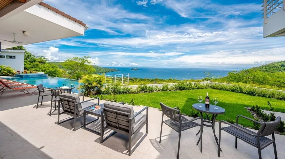 Modern patio with chairs, table, ocean view, and pool.