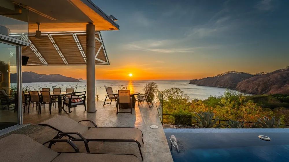 Sunset view from a patio with lounge chairs and a pool overlooking the ocean.